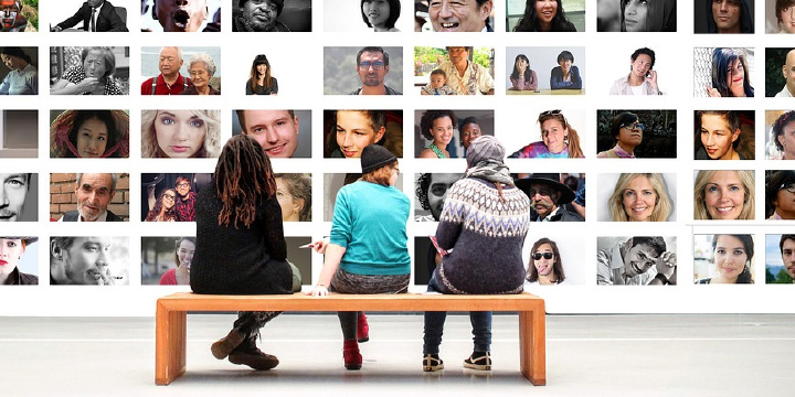 Three young people sitting on a bench looking at a wall of photographs