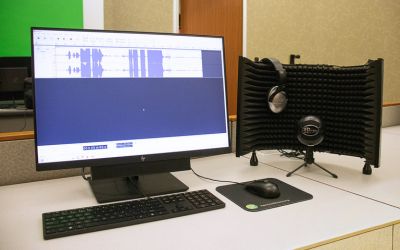 Audio recording setup with sound screen, headphones, microphone, and computer showing audio software.