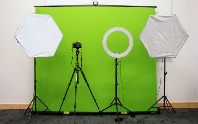 Various studio lighting and a DSLR camera set up on tripods in front of a green screen.