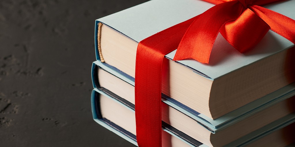 A stack of three books tied with a pretty red ribbon on a dark slate background.