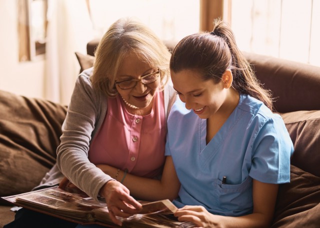 Shot of a nurse and a senior woman looking at a photo album together.