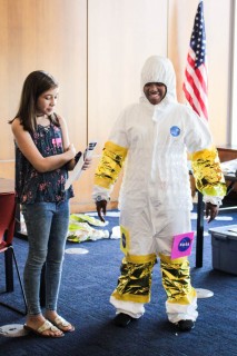 One teen presents their spacesuit design which the other teen is wearing,