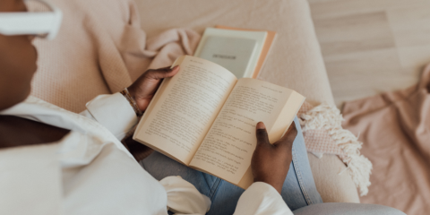 An over-the-shoulder view of an adult curled up on the couch reading.