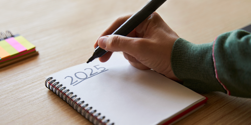 A close-up photo of a hand holding a pen. Beneath the pen is the text 