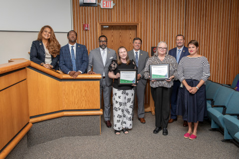 Eight individuals stand at the front of a boardroom and pose with an award.