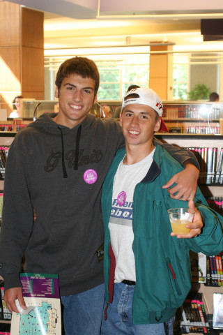 Two teens stand side-by-side with their arms wrapped around each other's shoulders. They smile at the camera. 