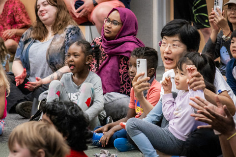 A close-up of young children and their caregivers smiling, clapping, and enjoying the performance happening in front of them (off camera).