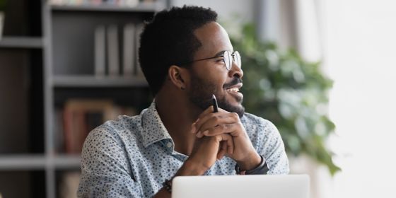 Man in front of a laptop looking off and smiling