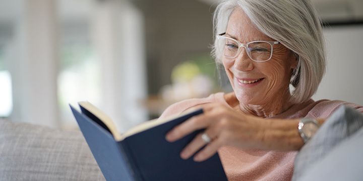 Senior woman sitting, reading a book, and smiling